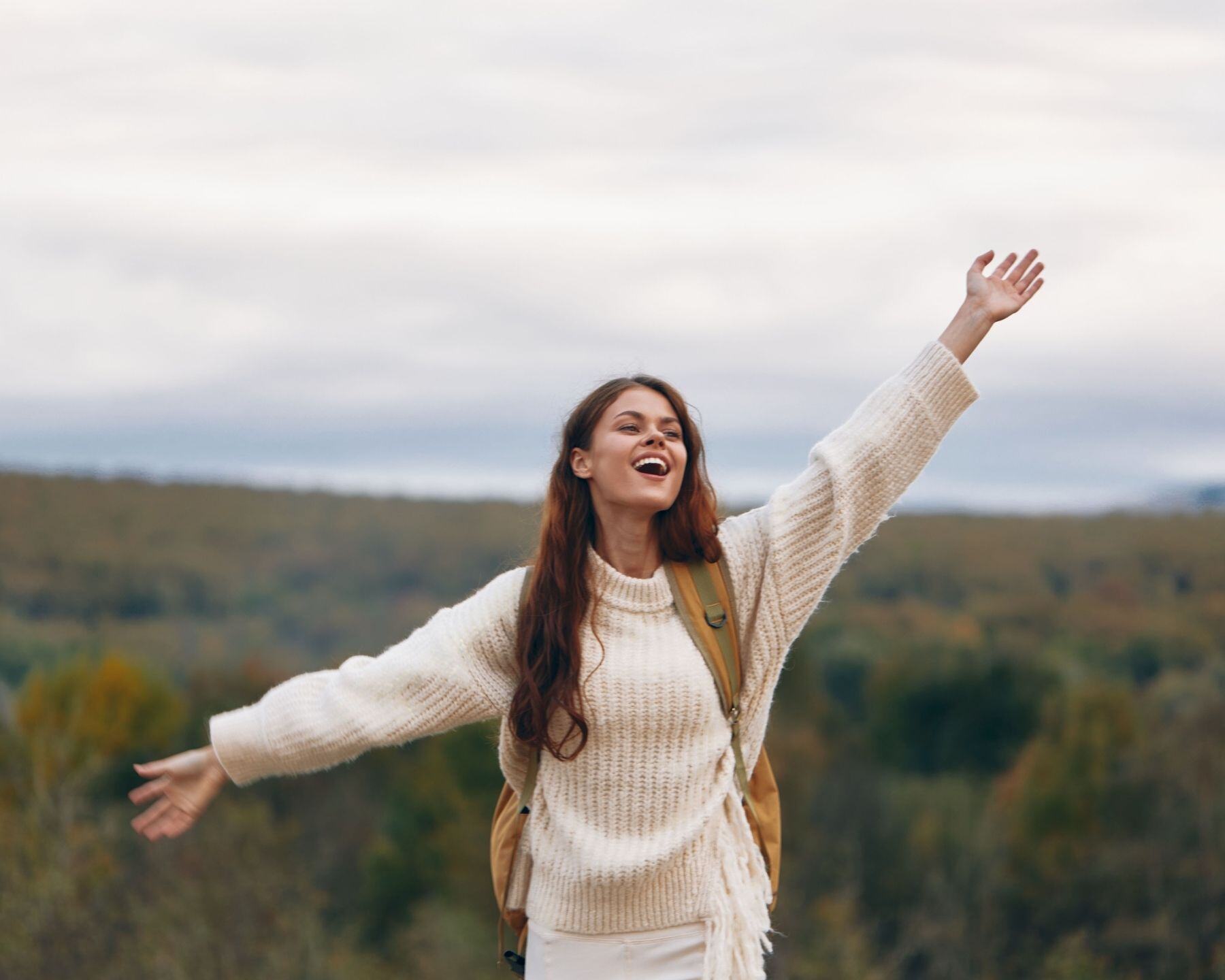 A young woman laughing with one arm raised, the countryside behind her