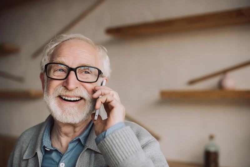 An older man in glasses smiling on the phone