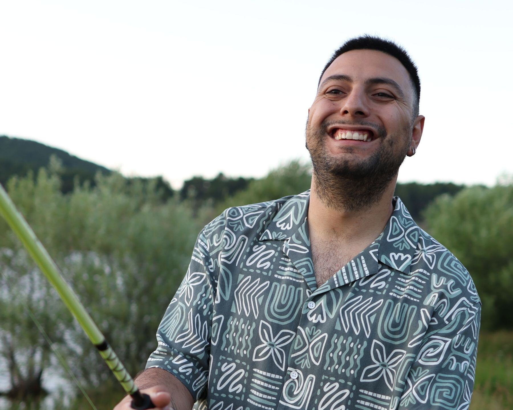 A man laughing outdoors in a patterned shirt