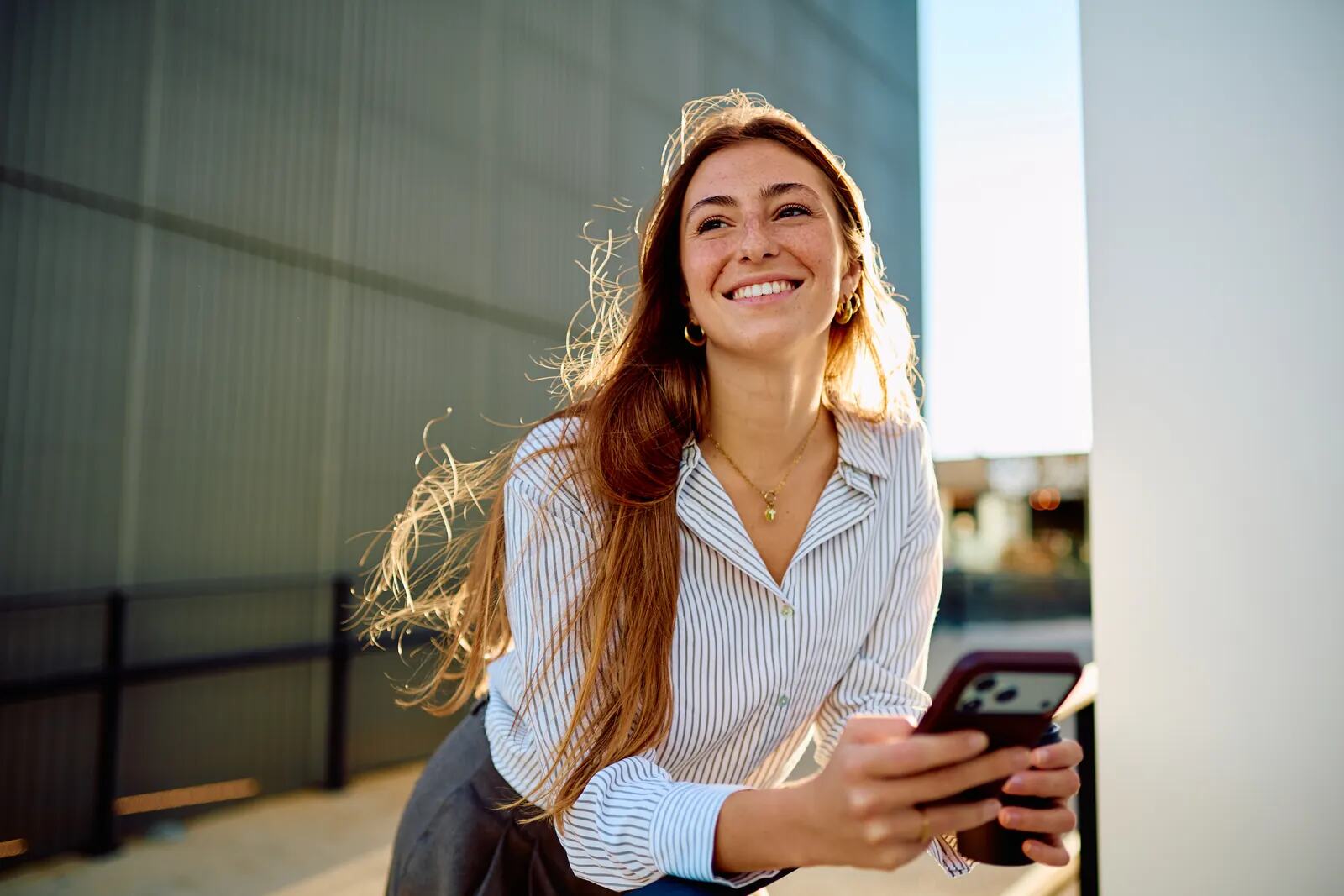 A young woman with long auburn hair smiling broadly in the city