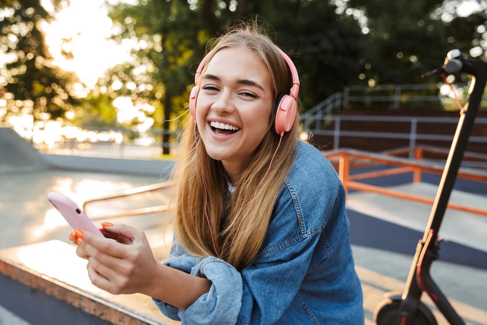 A young woman laughing, wearing pink headphones